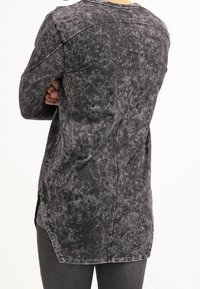 Maglietta nera a maniche lunghe con una texture invecchiata, aperture laterali e un orlo curvo. Caratterizzata da cuciture sulle spalle e un collo rotondo.