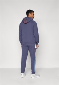 Sudadera azul marino con costuras naranjas, pantalones joggers a juego con rayas laterales en azul claro, confeccionados con una suave tela texturizada.