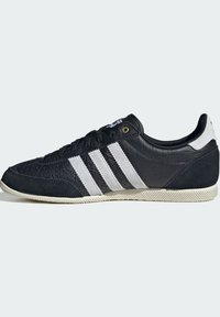 Black sneaker with white three stripes, suede and leather materials, rounded toe, textured rubber sole, and a classic design.