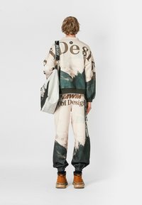 Sudadera y pantalones de cuello redondo en beige claro con un estampado de montaña; incluye una bolsa gris con correas negras y detalles gráficos, combinados con botas.