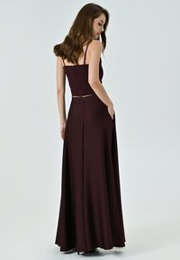 Longo vestito bordeaux con spalline sottili, corpino aderente, schiena scoperta e tasche laterali. Tessuto morbido, silhouette sagomata, design lungo fino al pavimento.