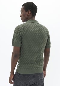 Zöld, rövid ujjú póló, texturált szőtt mintával és bordázott mandzsettával. Klasszikus gallérral és fitted derékkal rendelkezik.