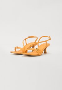 Sandales à talons en cuir jaune avec de fines lanières, boucle ajustable à la cheville, design à bout ouvert et un talon en bois modeste.