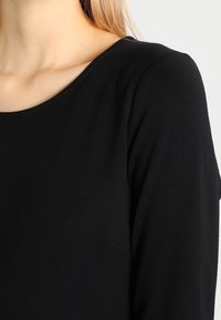 Czarny, długi rękaw top z okrągłym dekoltem i gładkim, teksturowanym materiałem. Posiada małą, dyskretną kieszonkę z boku.