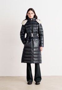 Μαύρο φούτερ με горизонтální κατασκευή, ψηλός γιακάς, ανοιχτό γκρι λεπτομέρειες στους ώμους, ζώνη στη μέση και φερμουάρ πλήρους μήκους.