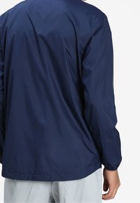 Navy windbreaker jacket with a lightweight, smooth texture and elastic cuffs, featuring a relaxed fit and a curved hemline.