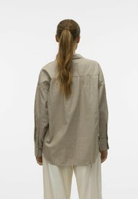 Rutet langermet skjorte i beige og brun, laget av lett materiale. Løs passform med krage og kneppede mansjetter, med en yoke-design.