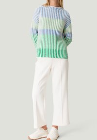 Gestreifter Strickpullover in Blau, Grün und Weiß, mit lockerer Passform und Rippstruktur. Kombiniert mit weißen, weiten Hosen und Sneakers.