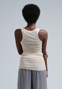 Lichtbeige tanktop met een aansluitend ontwerp, een ronde halslijn en dunne bandjes, gemaakt van zachte stof. Gecombineerd met grijze loszittende broek.