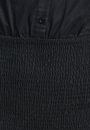 Črna obleka z prilegajočim bodicem in gumbi ter nabrano, teksturirano pasom. Gladka tkanina z rahlim sijajem.