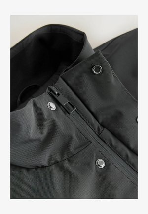 Juodas nepralaidus vandeniui striukės apykaklė su užtrauktuku ir spaudėmis; medžiaga turi tekstūrinį paviršių su subtiliomis vertikaliomis linijomis.