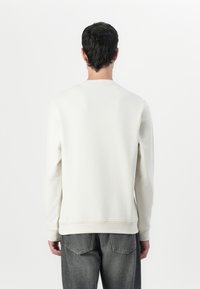 Lys kremfarget sweatshirt med lange ermer, rund hals, ribbestrikkede mansjetter og hem, brukt med mørkegrå jeans, minimalistisk design.