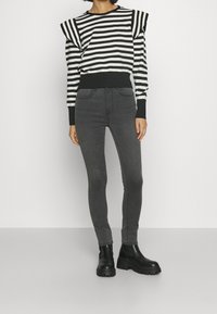 Top a maniche lunghe a righe bianche e nere con pieghe sulle spalle, abbinato a jeans skinny grigi e stivali neri chunky alla caviglia.