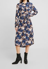 Blommig skjortklänning med lång ärm och bälte, med blå, vita och bruna blommönster. Bärs med svarta ankelboots.
