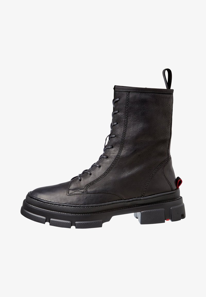Botte de combat en cuir noir à lacets avec semelle en caoutchouc épaisse et boucle au talon, présentant des détails cousus et un accent rouge à l'arrière de la semelle.