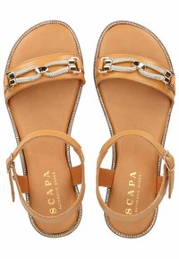 Helle Ledersandalen mit flacher Sohle, die dekorative Metallverbindungen und Strassakzente an den Riemen aufweisen. Verstellbarer Knöchelriemen inklusive.