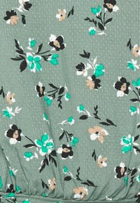 Tecido floral com um fundo verde suave, apresentando pequenas flores pretas, brancas e azul-turquesa. Textura lisa com padrões subtis e detalhes de pregas.