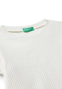 Bílá ribbená košile s kulatým výstřihem, krátkými rukávy a zelenou značkovou etiketou. Textura látky je měkká a pružná.