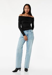 Sort off-shoulder langærmet bluse, parret med lyseblå lige ben jeans og sorte spidse hæle. Minimalistisk design, glat tekstur.