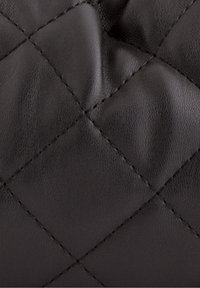 Černá prošívaná kůže s hladkým povrchem, zdobená prošíváním ve tvaru diamantu a jemním leskem. Žádné viditelné kovové prvky ani akcenty.