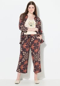 Tvådelad outfit med en brun mönstrad jacka och matchande korta byxor med palm- och geometrisk design. En krämfärgad topp under.