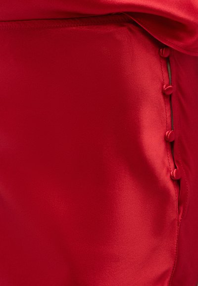 Close-up van rode satijnen stof met een rij bedekte knopen langs een naad, met een gladde textuur en lichte glans.