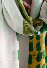 Écharpe en tissu doux avec des motifs abstraits verts, jaunes et rouges, drapée sur un fond uni.