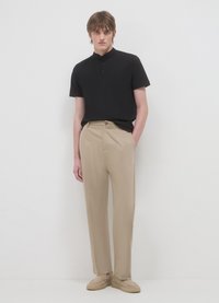 Polo nera a maniche corte con collo alto, abbinata a pantaloni beige a gamba dritta e scarpe slip-on beige chiaro.