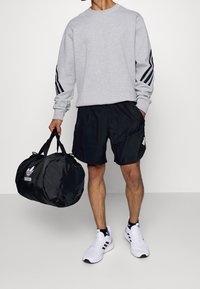 Grå sweatshirt med svarta ränder på ärmarna, svarta shorts, vita sneakers och en svart duffelväska med en vit logotyp.