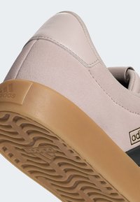 Světle růžový sneaker se semišovou texturou, gumovou podrážkou a detaily černého pruhu. Na patě se nachází vyražené logo značky.