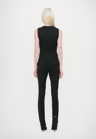 Top noir sans manches au design ajusté, associé à un pantalon noir slim avec une taille ceinturée et des chaussures à talons hauts.