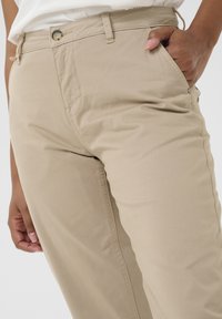 Beige, leichte Baumwollhosen mit Knopfverschluss, Seitentasche und glatter Textur mit genähten Nähten. Entwickelt für Komfort und Passform.