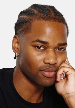 Portrait of a person with braided hair, wearing a black shirt. Features a gold hoop earring and is resting their chin on their hand.