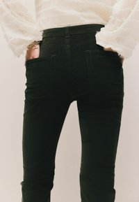 Jeans skinny neri in denim con vita alta, due tasche posteriori e cuciture a contrasto. La texture appare liscia e aderente.