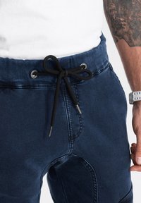 Pantalones jogger náuticos hechos de un material similar al denim, con un cordón negro, ojales plateados y detalles de costura visibles.