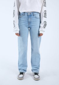 Jeans de mezclilla azul claro con cintura alta y corte relajado. Combinados con una camisa blanca de mangas largas que presenta diseños impresos en negro en las mangas.