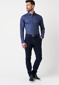 Marineblauwe langemouw overhemd met knopen en een gestructureerde kraag, gecombineerd met donkere spijkerbroeken en grijze sneakers. Uiterst gladde textuur, nauwsluitende pasvorm, minimaal ontwerp.