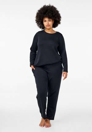 Schwarzes Loungewear-Set aus weichem Stoff mit langärmeligen Oberteil und tapered Hose, beide mit Seitentaschen und lockerem Schnitt.
