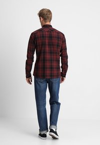 Rotes und schwarzes kariertes Hemd mit langen Ärmeln und Knopfkragen. Kombiniert mit blauen Jeans und schwarzen Turnschuhen mit weißen Sohlen.