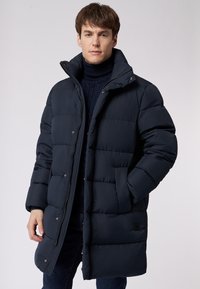 Donsjack in donker marineblauw, met een hoge kraag, ritsluiting en drukknoopsluiting. Dikke voering met een quilty patroon en zijzakken.