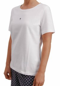 Camiseta blanca de algodón con mangas cortas y cuello redondo. Presenta un pequeño logo azul oscuro en el pecho. Textura suave, corte recto.