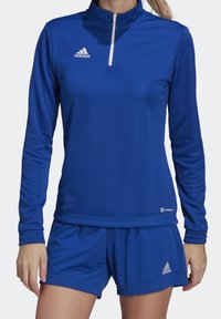 Camiseta deportiva azul de manga larga con cremallera de un cuarto y logo blanco; combinada con pantalones cortos azules a juego con cintura elástica y acento de logo.