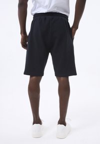 Pantalones cortos texturizados color azul marino con cintura elástica y bolsillos laterales, combinados con zapatillas blancas. El corte es justo por encima de la rodilla.
