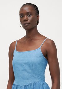 Vestido de denim azul claro con tirantes finos, escote cuadrado y falda acampanada. Textura suave con detalles de costura visibles.