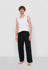 Vit bomullstopp och lösa svarta byxor med elastisk midja, stående på en enkel bakgrund.