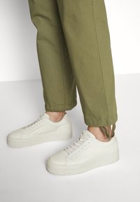 Witte leren sneakers met een gestructureerde afwerking, platte zool en vetersluiting, gecombineerd met olijfgroene broek met een omgeslagen zoom.