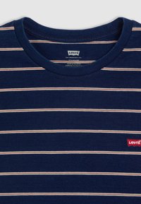 Tamsiai mėlynas marškinėliai su horizontaliomis baltomis ir raudonomis juostelėmis, apvaliu dekolte ir mažu raudonu Levi's logotipo pažeidimu kairėje pusėje.