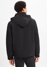 Zwarte capuchonjas met een slanke, gladde textuur. Heeft een iets losse pasvorm, zijzakken en een logopatch op de linkermouw.