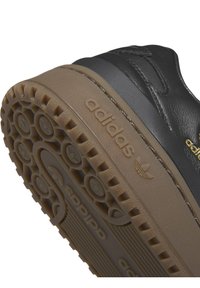 Svart lädersneaker med en tjock gummisula. Har präglad logotyp och en strukturerad mönstring för bra grepp.