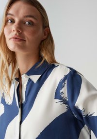 Hemd mit Knopfleiste in Marineblau und Weiß; zeigt ein abstraktes Pinselstrichmuster, einen Hemdkragen, lange Ärmel und eine glatte Stoffstruktur.